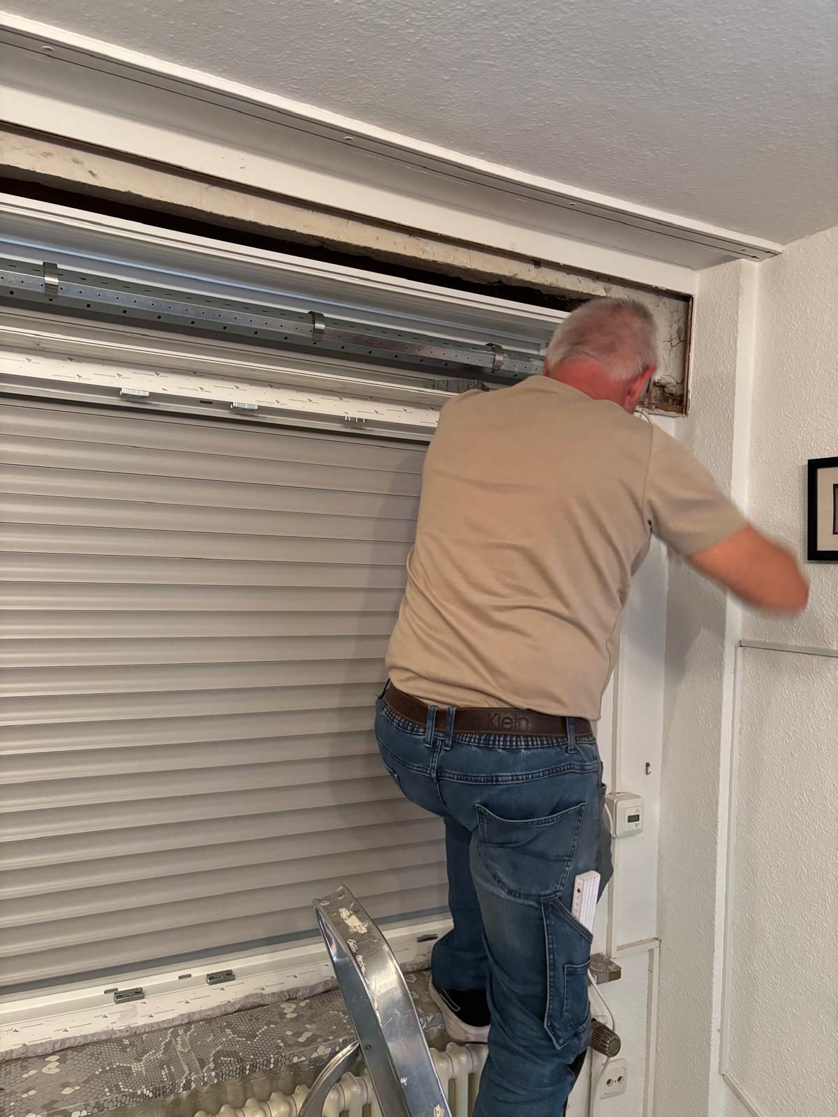 Monteur arbeitet am Rollladenkasten über einem Fenster